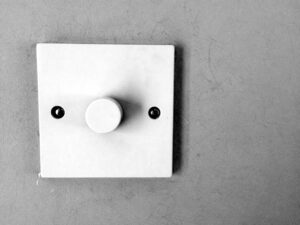 White wall-mounted light switch with a central round dial and two small black screws on either side.