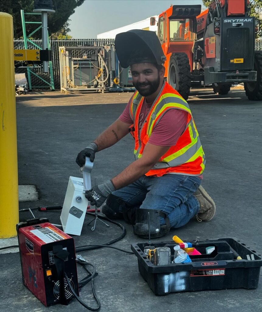 A Prairie Electric electrician wearing safety gear kneels on the ground, handling and installing electrical equipment in Vancouver, WA.