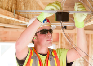 A construction worker in a high-visibility vest, hard hat, and safety glasses is installing electrical wiring in a building frame, much like an experienced electrician in Vancouver, WA.