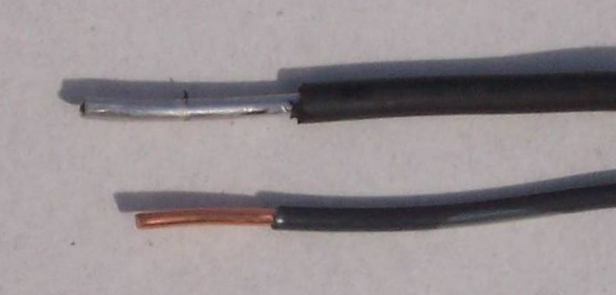 Close-up of two black wires with exposed ends on a white background, one with copper and the other with aluminum visible.