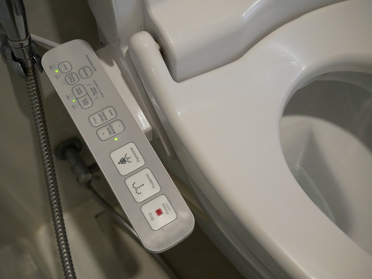 Close-up of a modern toilet with a control panel featuring various buttons for functions like bidet, spray, and seat heating. The sleek design emphasizes both comfort and convenience.