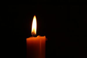 A single candle is lit, glowing brightly in the dark, with a visible wick and melted wax drippings. The background is completely black.