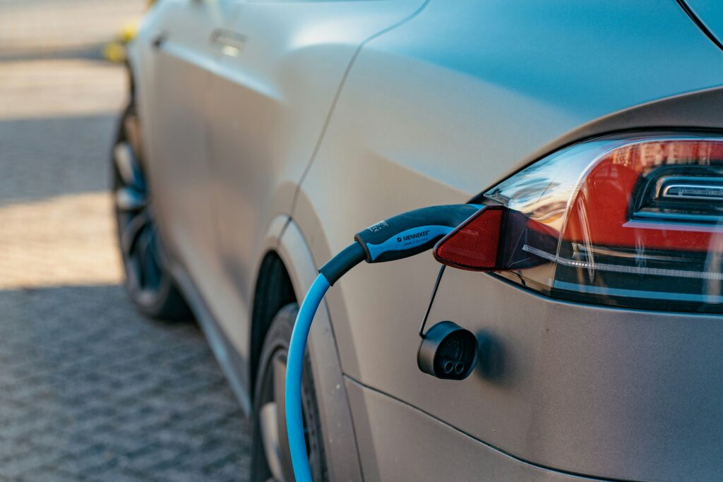 An electric car is being charged, with the charging cable connected to the rear of the vehicle. The car is parked on a paved surface.