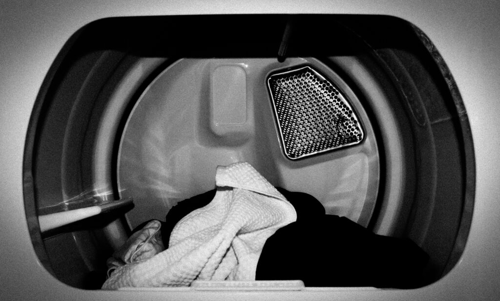 A view inside an open dryer with a pile of clothes, featuring white and dark garments, and a visible lint trap on the inner wall.