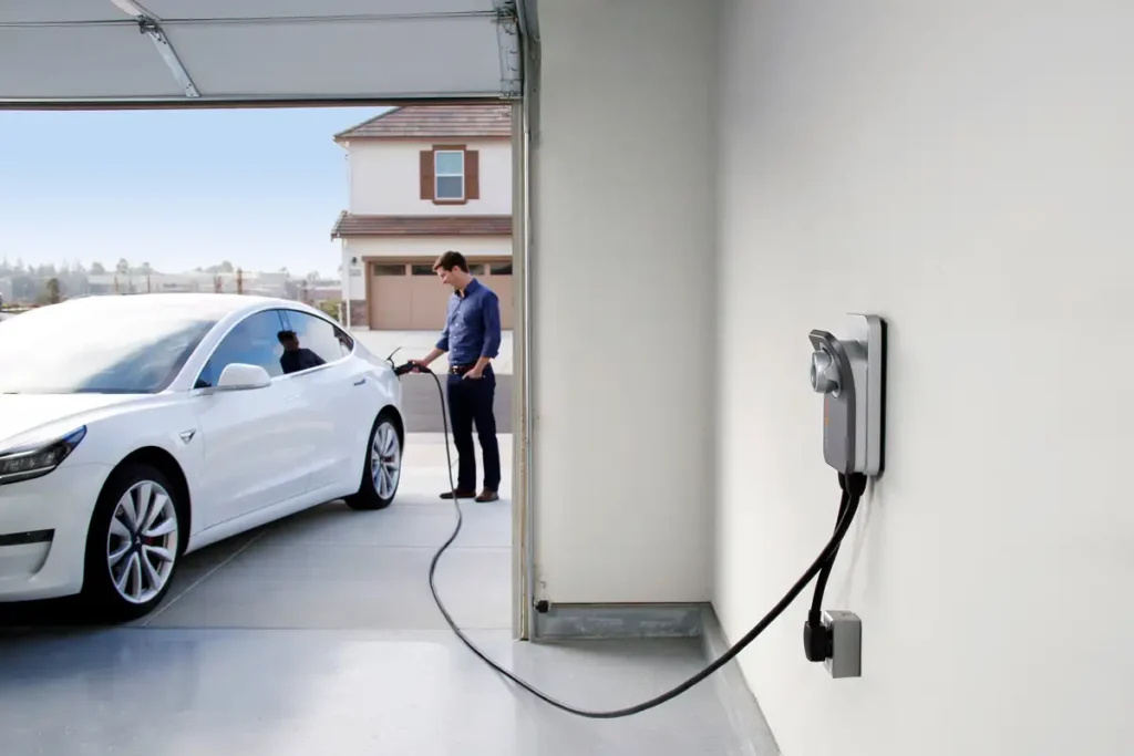 Electric car charging station installed in a home garage, being used by a man to charge his EV.