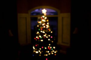 A dimly lit room with an out-of-focus Christmas tree adorned with multicolored lights and a star on top.