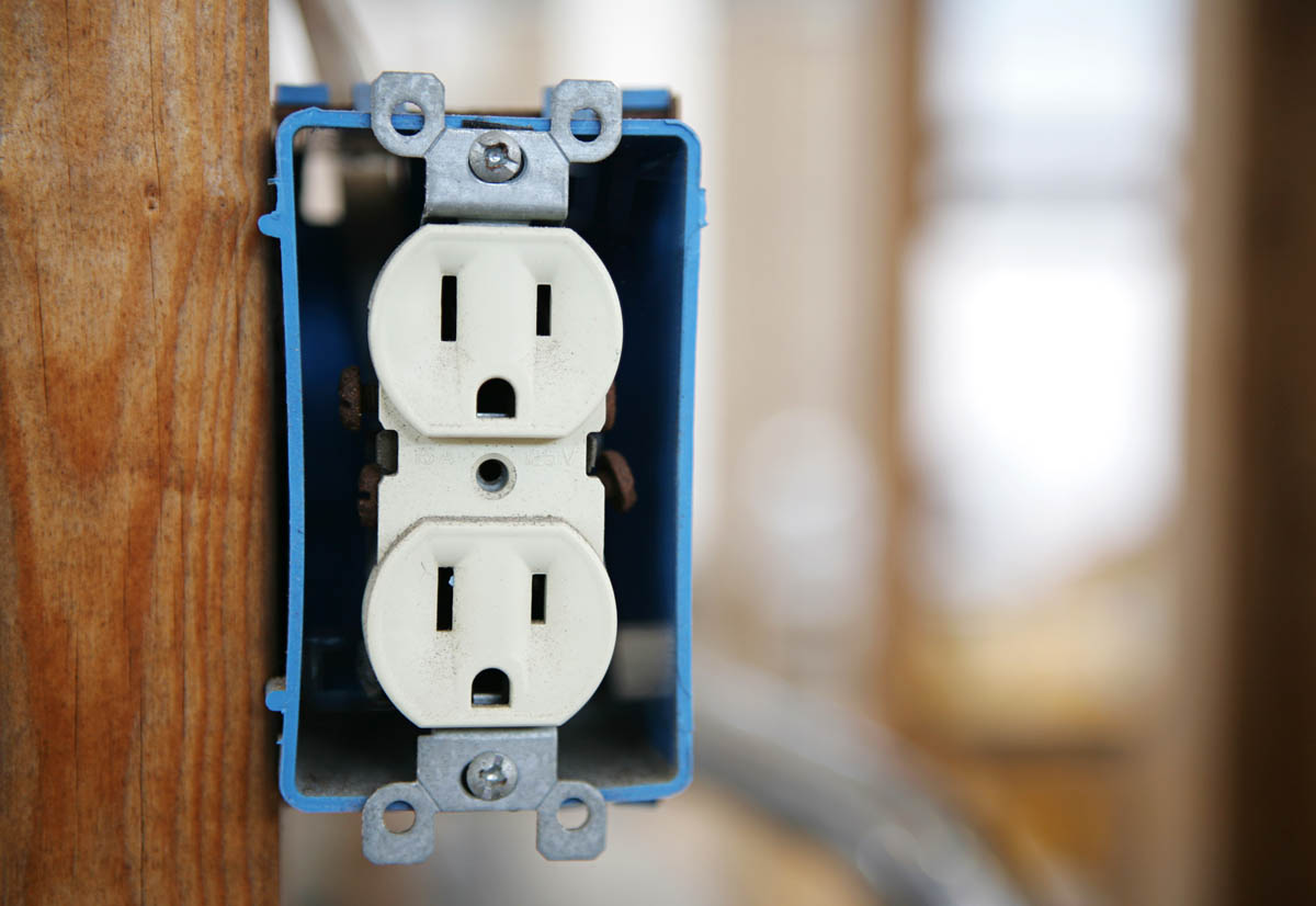 Close-up of an electrical outlet inside a blue junction box attached to a stud