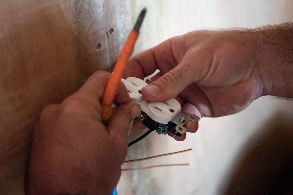 Hands meticulously completing the electrical installation of a new outlet with the help of a screwdriver.