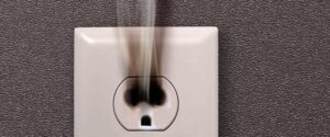 A close-up of a wall electrical outlet, with visible black smoke and burn marks indicating overheating or a possible fire hazard. Contact a Vancouver electrician immediately to address this critical electrical issue and ensure your safety.