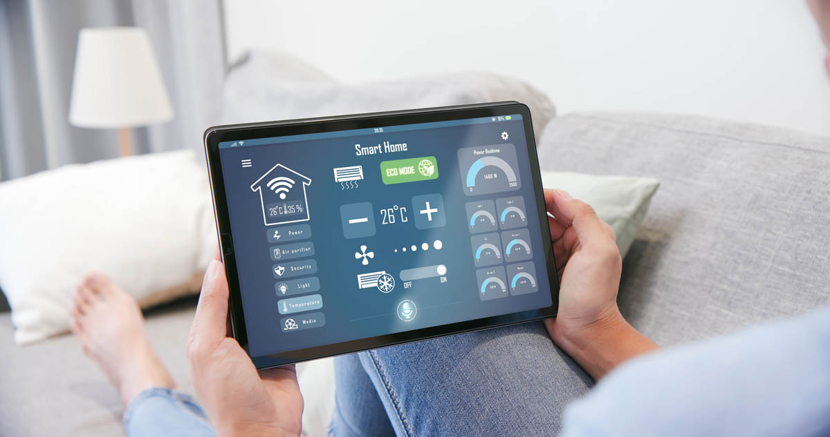 Person holding a tablet with a smart home control interface, displaying temperature, fan control, lighting, and other home automation options on the screen—making it as easy as knowing how to read your electric meter.