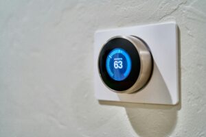 A round digital thermostat mounted on a white wall displays a current temperature of 63 degrees Fahrenheit.