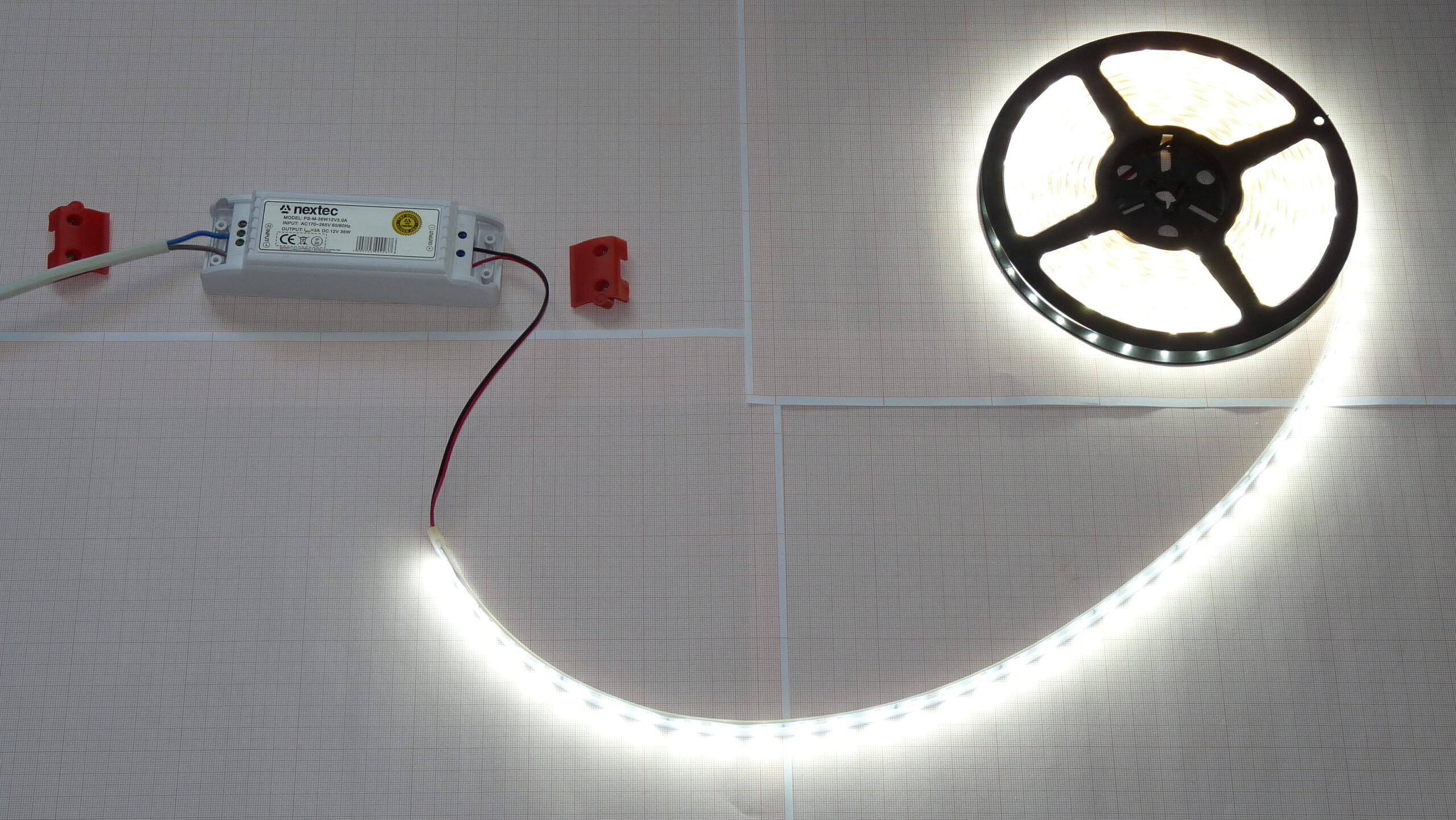 LED strip light partially unrolled and illuminated, connected to a power supply mounted on a wall grid.